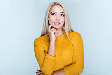 Maybe I should try something new! Beautiful young woman with blond hair keeping hand on chin while standing against grey background