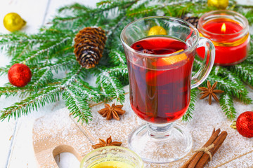 New Year's mulled wine in a glass on the background of twigs, candles and garlands.