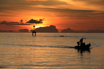 beautiful scenery of red dramatic sunset with lighthouse and sailing boat on island in ocean