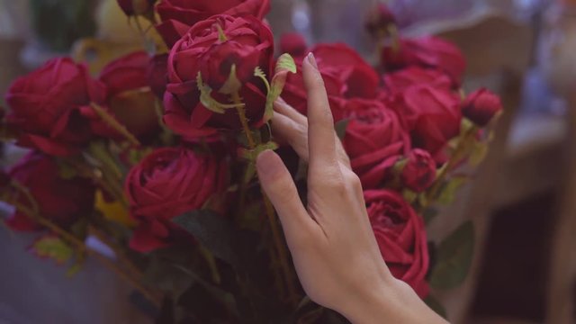 flower shop. A large vase with a bouquet of burgundy peonies. a young woman chooses flowers. touches the buds with his hand. 4k