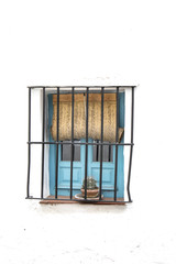 ventana pintada de azul con barrotes de hierro forjado y persiana de esparto en pared blanca encalada © tingitania