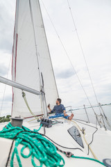 man sits on bow of sailing yacht and holds binoculars