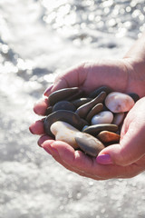 Sea stones in hands on the beach in the summer