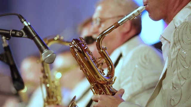 Close-up. A man in the foreground starts playing the saxophone with the other members of the brass band.