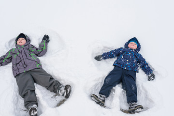 Fototapeta na wymiar Two little siblings kid boys in colorful winter clothes making snow angel, laying down on . Active outdoors leisure with children in . Happy brothers