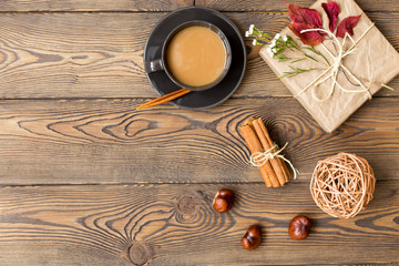 Autumn composition. Coffee with milk, gift, autumn leaves, cinnamon sticks and chestnuts on wooden background.