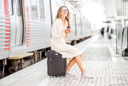 Young elegant woman waiting with luggage for the train departure at the railway station