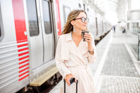 Portrait of a young elegant woman standing with coffee cup near the train at the railway station