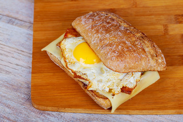 Hamburger with bacon, egg and french fries on a wooden cutting board.