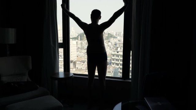 Silhouette of man stretching arms and admire view from window
