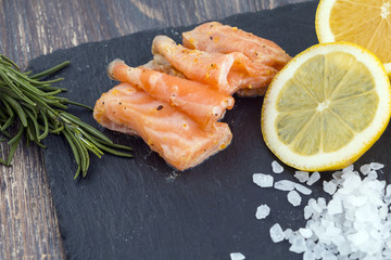 Fermented salmon on slate with sea salt, lemon, rosemary. Closeup.