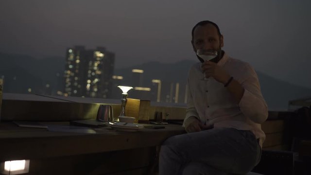 Portrait of happy man raising toast with drink on terrace in bar at night
