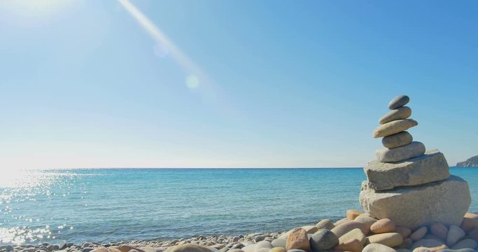 Waves landing on stone beach. Meditation, stone pyramide. Clear blue water.