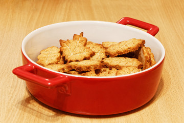 Red bowl with homemade crunchy cookies in the form of leaves on the wooden table. Shallow focus.