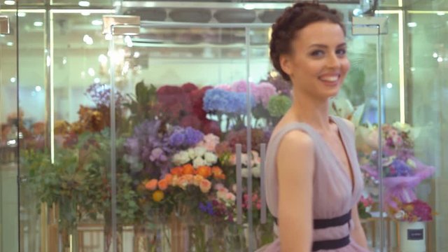 flower shop. young attractive brunette girl stands near a fridge with flowers. florist in the evening's casual dress on the background of a large number of flowers. professional model in the image of