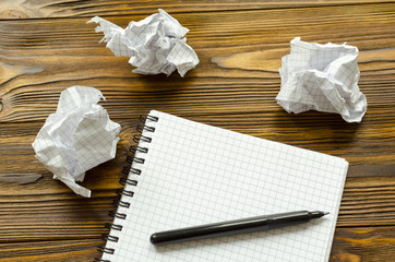 Notepad, pen and crumpled sheets of paper on wooden table