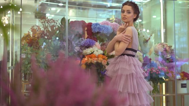 flower shop. young attractive brunette girl stands near a fridge with flowers. florist in the evening's casual dress on the background of a large number of flowers. professional model in the image of