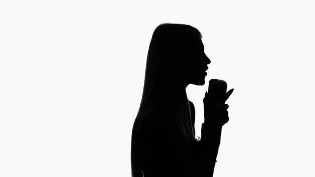 Vocalist in a dress is singing into a retro microphone. Silhouette. Side view. White background