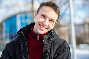 Portrait of handsome young man in red in a sunny snowy day. Winter lifestyle portrait of handsome young man walking in the snowy park