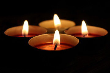 Obraz na płótnie Canvas Small candles burning flames on black background at night