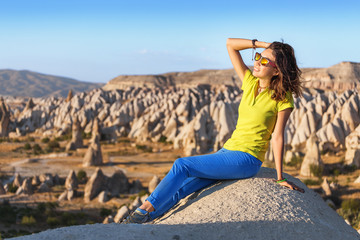 Naklejka premium A young tourist sitting on a mountain top and looking at the sunrise in Cappadocia at red valley. Tourism and travel in Turkey concept