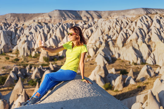 Happy young woman taking selfie with her smartphone with Cappadocia landscape at the background, Goreme, Turkey