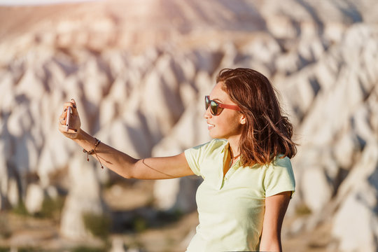 Happy young woman taking selfie with her smartphone with Cappadocia landscape at the background, Goreme, Turkey