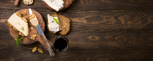 Assorted cheeses on wooden boards plate, bread and wine on dark wooden background, top view, flat...