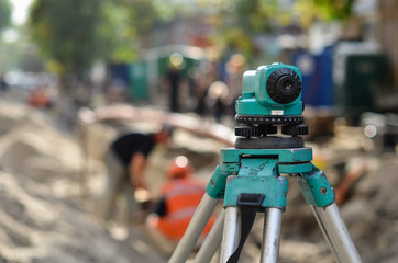 optical level on background of workers dig pit