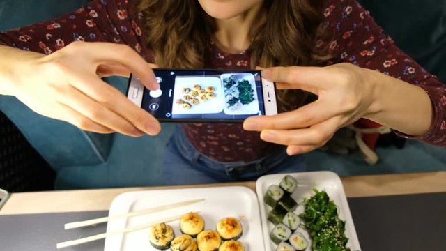 Woman photographing food served in sushi bar with mobile phone. Food and drink concept