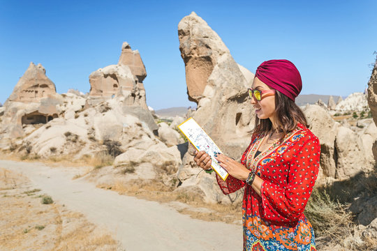 A happy young tourist eastern asian girl in traditional clothes travels among cappadocia landscape and cave towns at summer and reading map