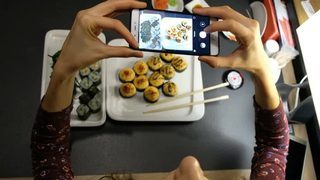 Woman photographing food served in sushi bar with mobile phone. Food and drink concept