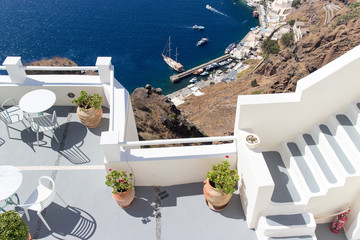 A balcony with plants in jugs and a view on a sea, mountains and city with white houses