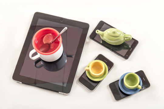 The smartphone and tablet are used as a stand for cups with tea. Toy set of dishes. Broken phone.