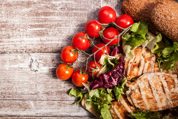 Delicious fresh grilled chicken on wooden board next to healthy bread, tomatoes and salad. Healthy lifestyle and eating