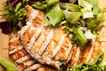 Close up on grilled chicken breast on fresh cut salad next to a bunch of tomatoes on a wooden board