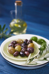 Plate with olives and oil on color wooden background