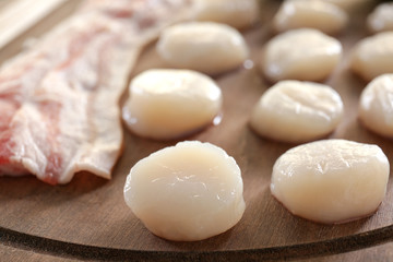 Fototapeta na wymiar Wooden board with raw bacon and scallops, closeup