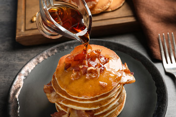 Pouring honey onto pancakes with bacon on plate