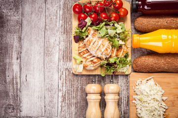 Delicious grilled chicken on wooden board next to healthy bread, tomatoes and salad. Copy space...