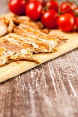 Delicious Fresh sliced grilled chicken breast on wooden board next to a bunch of tomatoes. Healthy dinner and lifestyle 