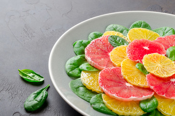 Salad made of orange and grapefruit slices and spinach leaves on a gray plate on dark stone background. Close-up, horizontal image