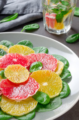 Salad made of orange and grapefruit slices and spinach leaves on a gray plate and glass of water on dark stone background. Close-up, vertical image