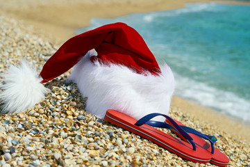 Santa Claus hat and flip flops оn sand.
