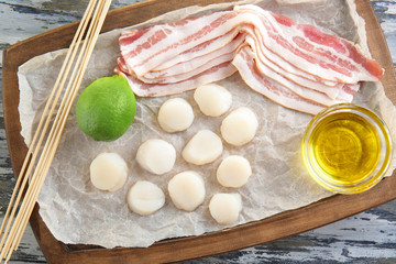 Wooden board with raw bacon and scallops on table