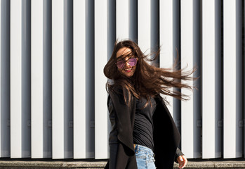 Street portrait of happy young model with hair blowing in wind walking at the street