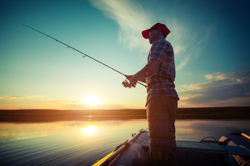 Man fishing in a pond from a boat at sunset