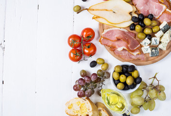 Appetizer, italian antipasto, ham, olives, cheese, bread, grapes, pear on white wood background