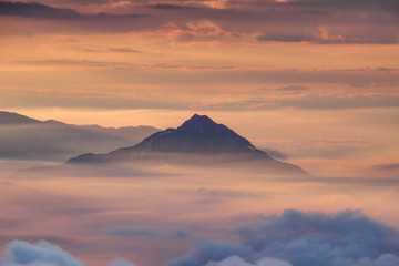 Lonely conical mountain towers above autumn morning mist and sea of low clouds illuminated with red color light by rising sun, Storzic peak, Kamnik Savinja Alps, Kranjska, Gorenjska, Slovenia, Europe