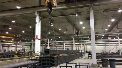 Heavy duty chains linked to ceiling lifts move large tubes of steel in preparation for shipping onto trucks. - Powered by Adobe
